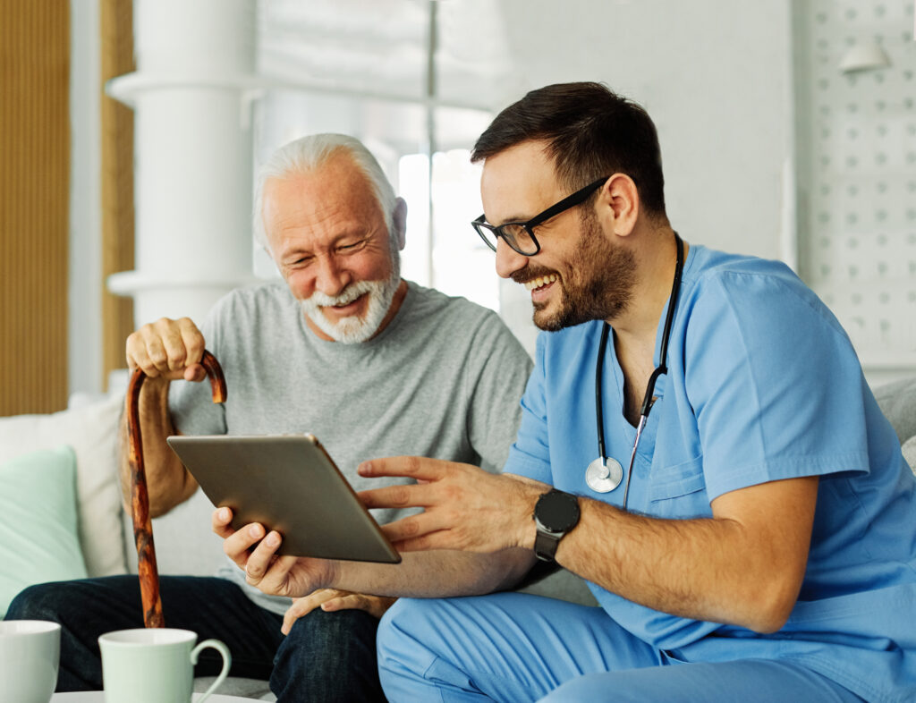 Doctor or nurse caregiver showing a tablet screen to senior man and laughing at home or nursing home